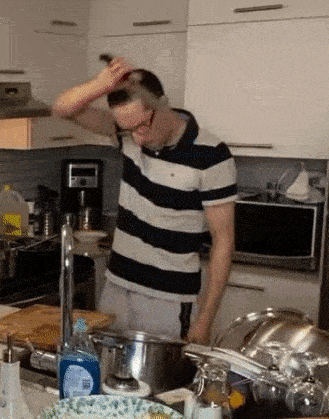 a man in a striped shirt is washing his hair in a kitchen sink