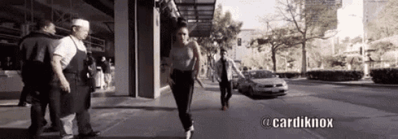 a woman is walking down a city street with a car behind her