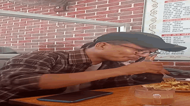 a man wearing glasses and a hat sits at a table in front of a sign that says ' menu ' on it