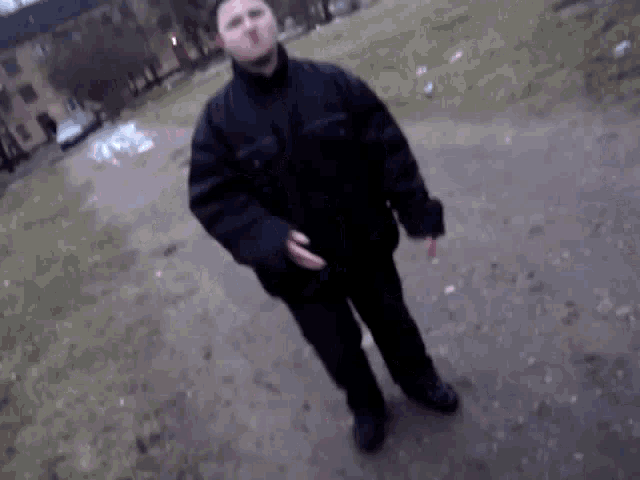 a man in a black jacket is standing on a dirt path .