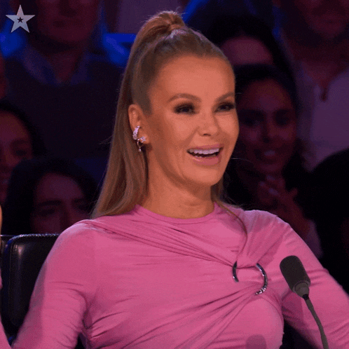 a woman wearing a pink top is smiling in front of a microphone