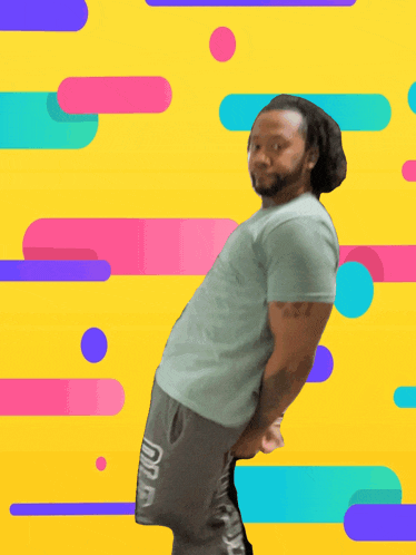 a man in a blue shirt and grey shorts stands in front of a yellow and pink background