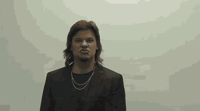 a man in a suit and a necklace is making an angry face