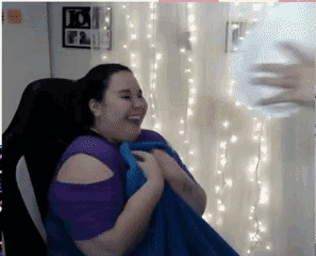 a woman in a purple shirt is sitting in a chair holding a blue blanket