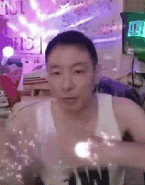 a man in a white tank top is sitting in a room holding a glass .