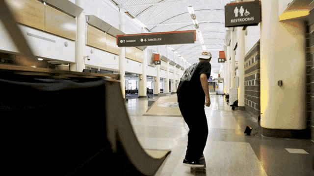 a man is skateboarding in a hallway with a restrooms sign above him