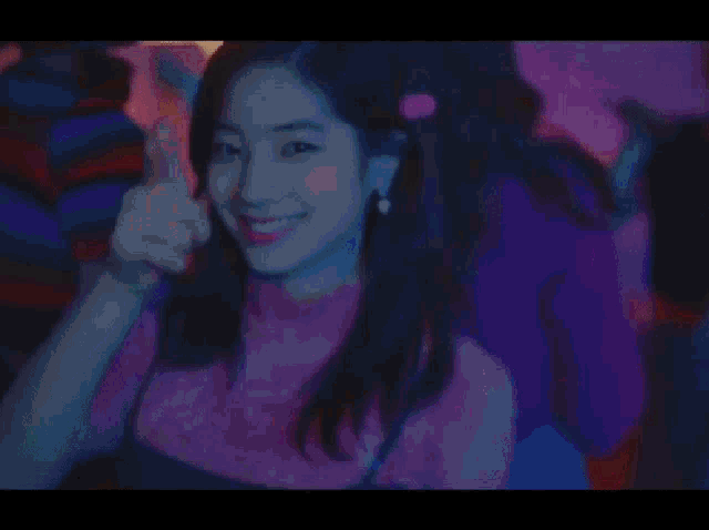 a woman in a pink shirt is smiling and giving a thumbs up at a party .
