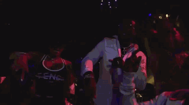 a group of men are dancing in a dark room and one of them is wearing a shirt that says ' sens ' on it