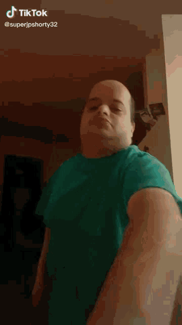 a bald man in a green shirt is standing in a dark room with a tiktok watermark