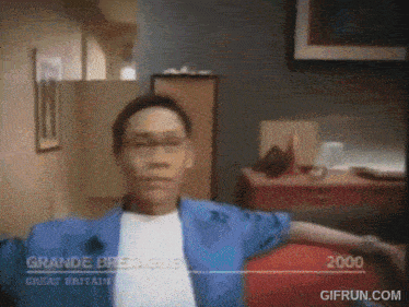 a man in a blue jacket is sitting in a living room with the year 2000 on the bottom of the screen