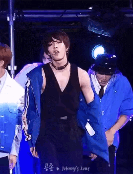 a man wearing a black tank top and a blue jacket is dancing on a stage in front of a johnny 's zone sign
