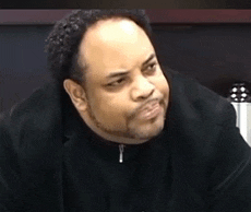 a man with a beard is wearing a black jacket and making a funny face