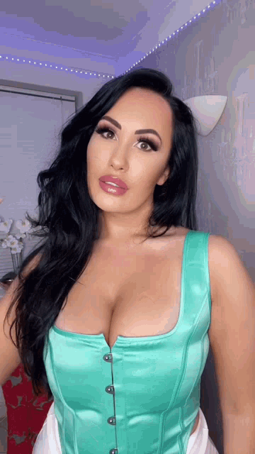 a woman with long black hair is wearing a teal corset top .