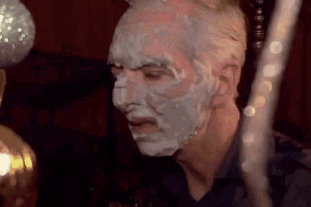 a man with a shaving cream mask on his face is sitting at a table .