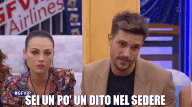 a man and woman are sitting in front of a sign that says " sei un po ' un dito nel sedere "