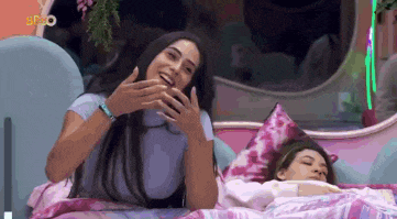 a woman is laughing next to another woman who is laying in bed .