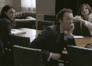 a man in a suit sits at a table with a woman behind him