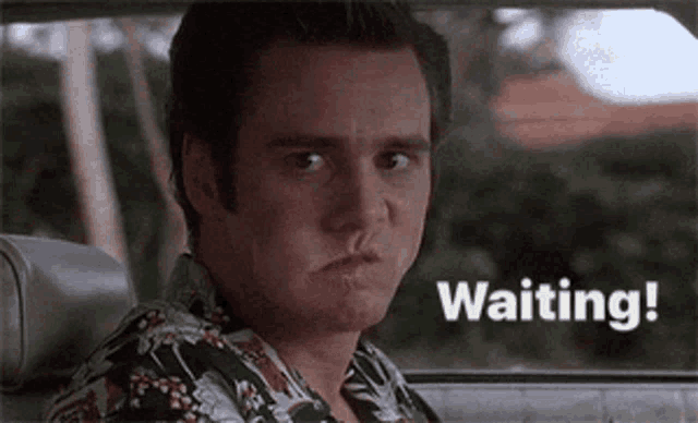 a man is sitting in the back seat of a car with the words `` waiting '' written on the screen .