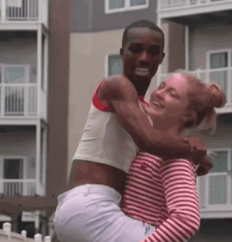 a woman in a red and white striped shirt is hugging a man in a white crop top