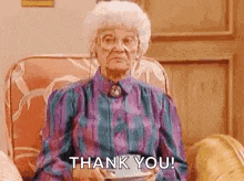 an elderly woman is sitting in a chair holding a cup and saying `` thank you '' .