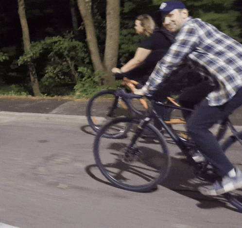 a man in a plaid shirt is riding a bike next to a woman in a black shirt