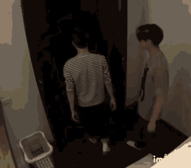 two men are standing next to each other in a dark room with a laundry basket in the background .
