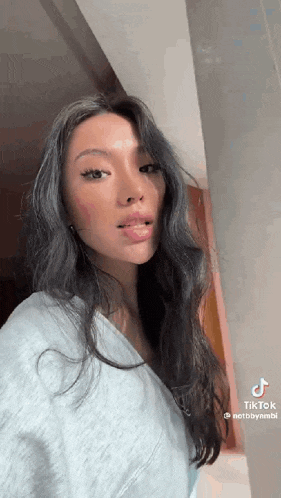 a woman with long dark hair is standing in front of a wall and looking at the camera .