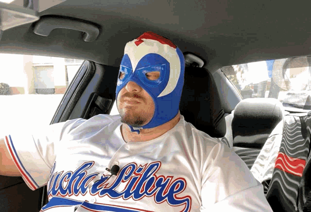 a man wearing a mask and a jersey that says libre is sitting in a car