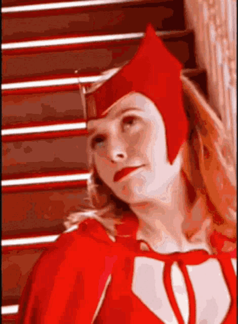 a woman in a red cape and hat is standing in front of some stairs .