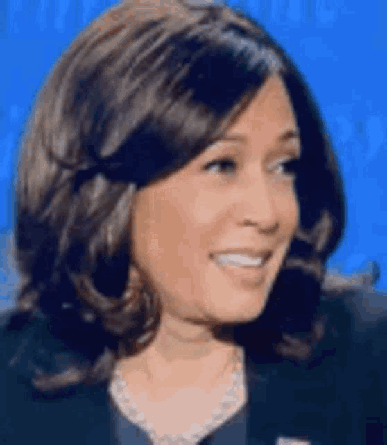 a close up of a woman 's face with a blue background . she is smiling and wearing a necklace .