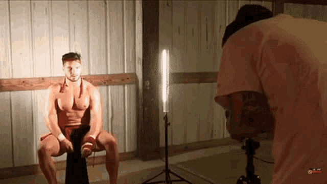 a shirtless boxer is being photographed by a man in a pink shirt ..