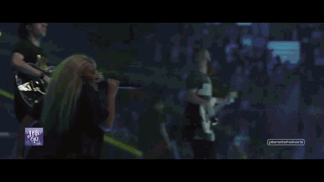 a woman sings into a microphone while a man plays a guitar in front of a crowd