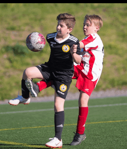 two young boys playing soccer one of whom is wearing a jersey that says adidas on it