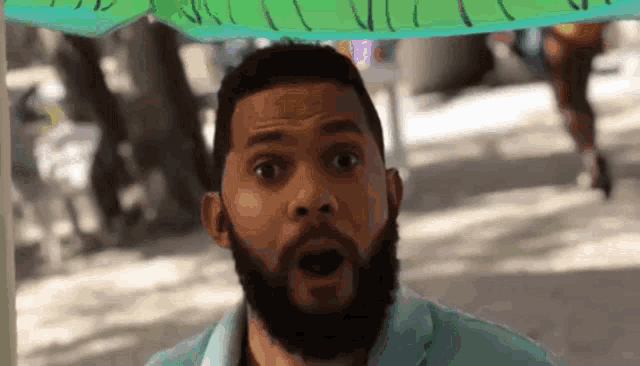 a man with a beard is standing under an umbrella with his mouth open .