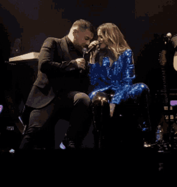 a man singing into a microphone next to a woman in a blue sequined outfit