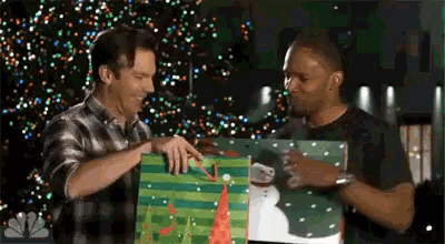 two men are standing next to each other holding a christmas present .