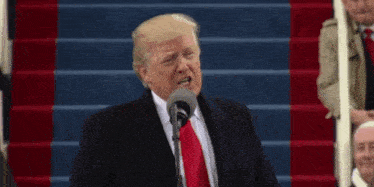 donald trump speaking into a microphone while wearing a suit and tie