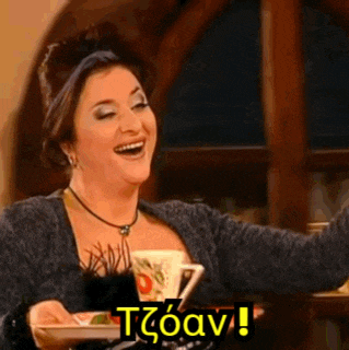a woman is sitting at a table with a plate of food and a cup of coffee and laughing .