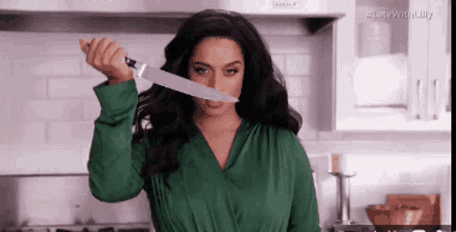 a woman in a green shirt is holding a large knife to her mouth