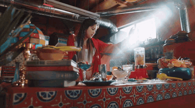 a woman in a red shirt is standing at a counter with a blender and a bowl of food