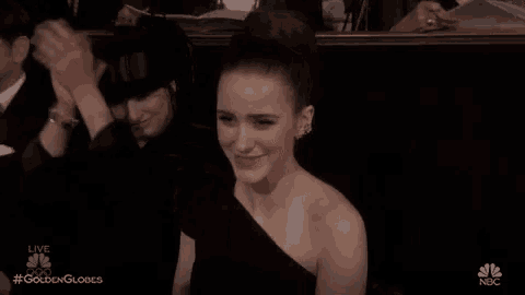 a woman in a black dress is sitting in a theatre applauding a man .