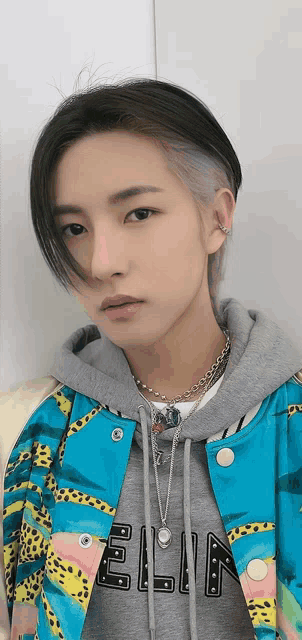 a young man with a shaved head is wearing a colorful jacket and a gray hoodie .