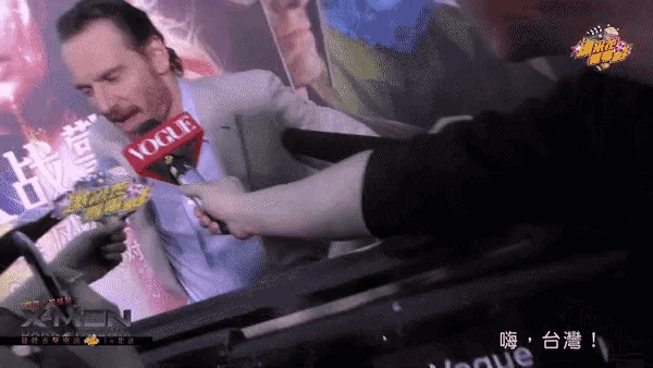 a man talking into a vogue microphone in front of a xmen poster