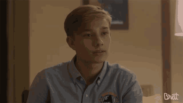 a young man wearing a blue shirt with the word brat on the bottom