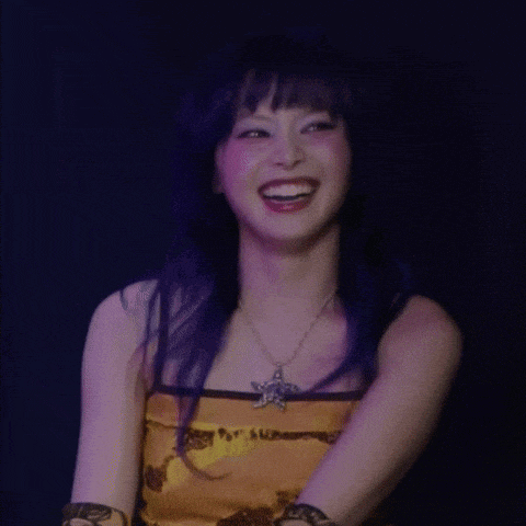 a woman with purple hair is laughing with her eyes closed and wearing a star necklace .