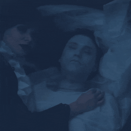 a woman laying next to a dead man in a coffin with his eyes closed