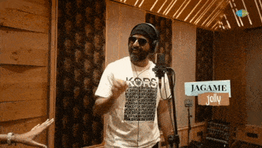 a man wearing headphones and a michael kors t-shirt sings into a microphone