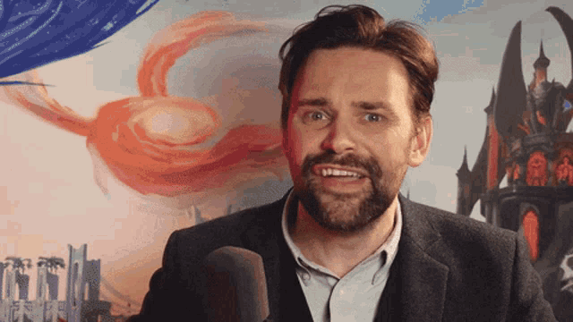a man with a beard is talking into a microphone in front of a painting