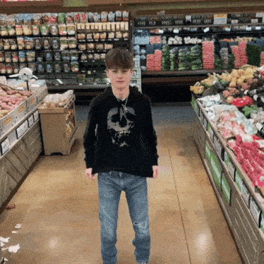a young boy wearing a black hoodie with a skull on it is standing in a grocery store