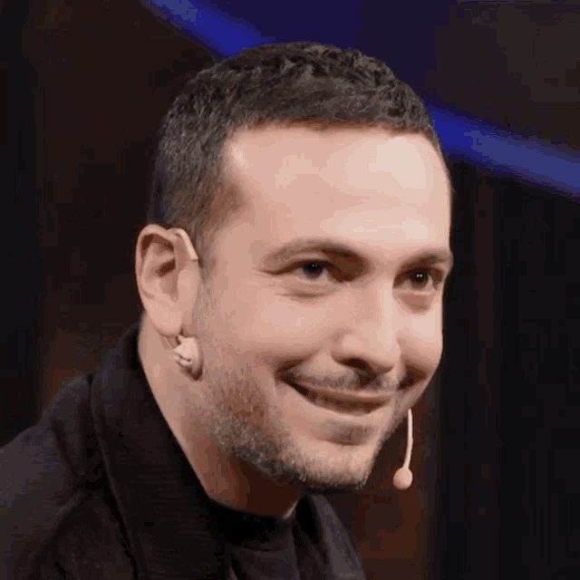 a man with a beard is smiling with a microphone hanging from his neck